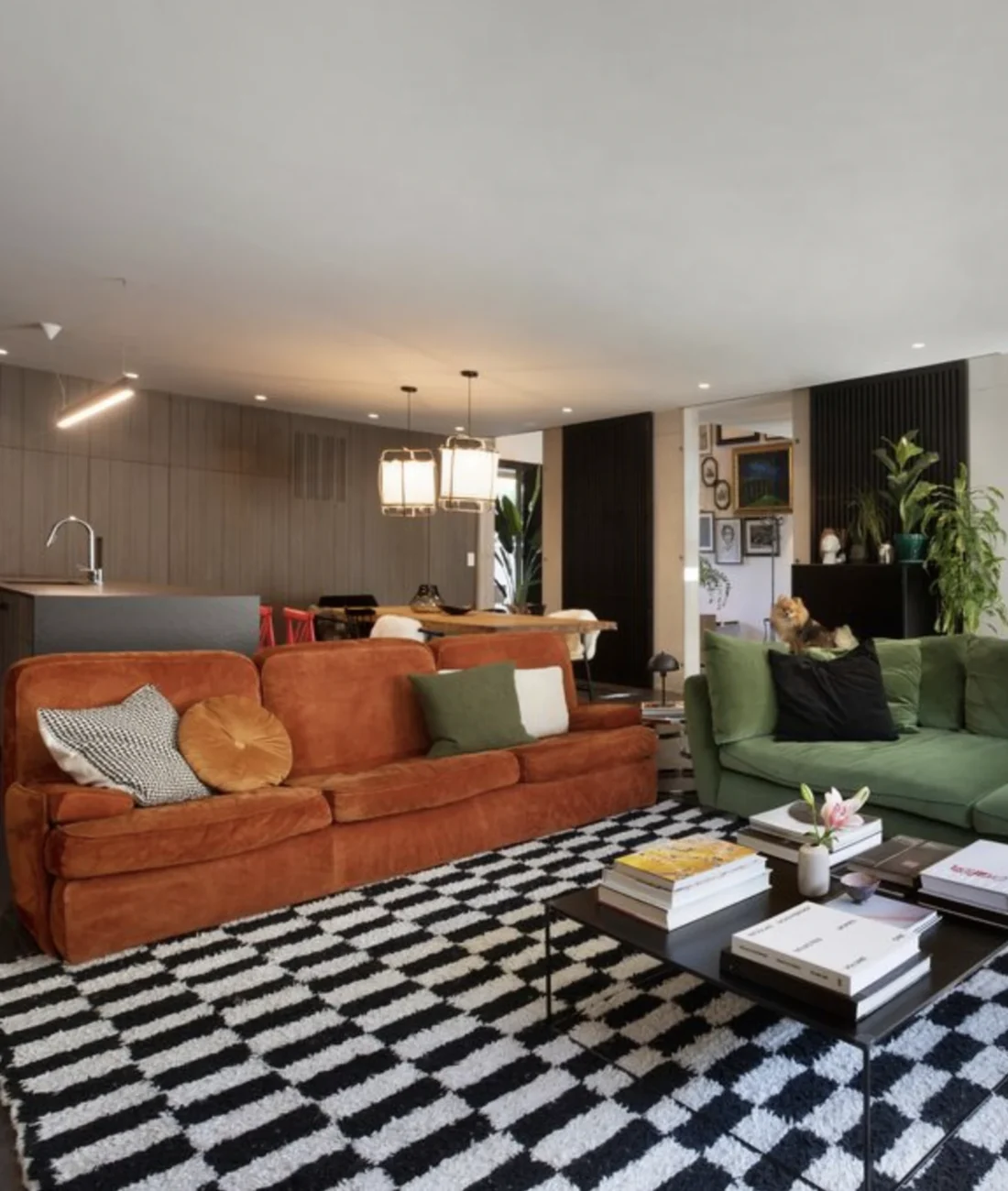 Salon contemporain inspiré des années 1970 avec canapé vert olive, fauteuils orange, tapis noir et blanc et meuble en laiton.