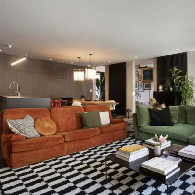 Salon contemporain inspiré des années 1970 avec canapé vert olive, fauteuils orange, tapis noir et blanc et meuble en laiton.