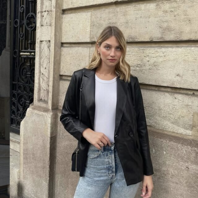Femme blonde en blazer en cuir noir, t-shirt blanc et jean clair, dans un look clean girl